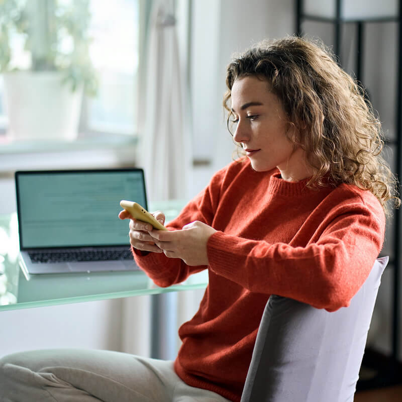 A woman sitting at her home office desk looking at her phone