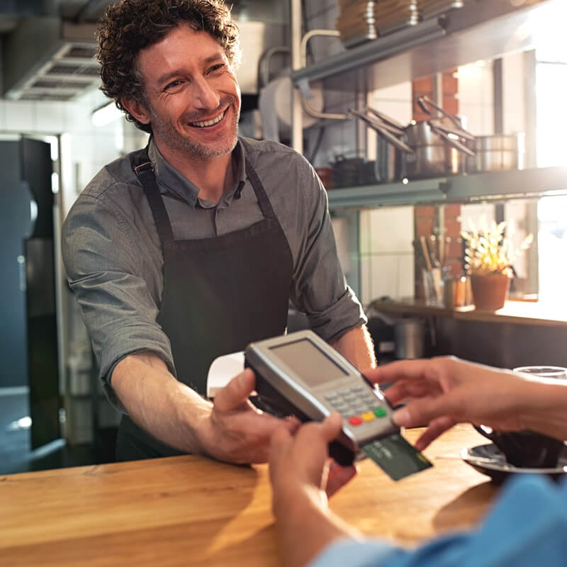 A smiling cashier hands someone a credit card reader.