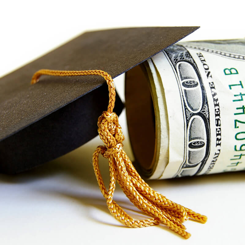 A mortar board leaning on a stack of money.