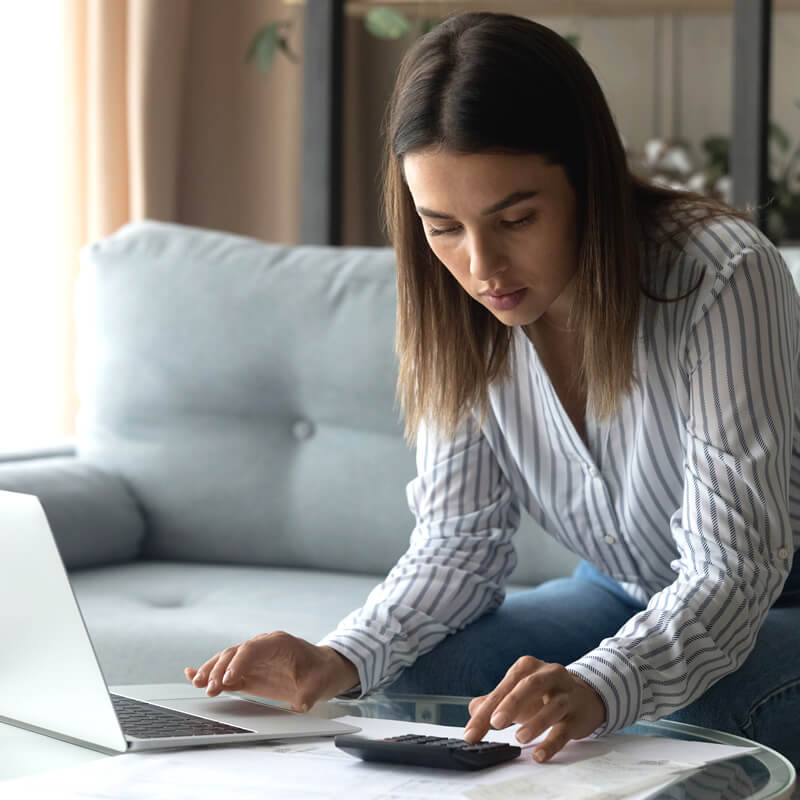 A focused woman using a calculator while sitting on her sofa.