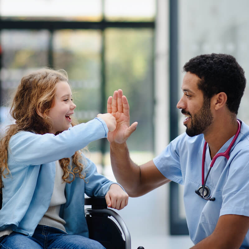 A doctor gives a high five to a girl in a wheelchair