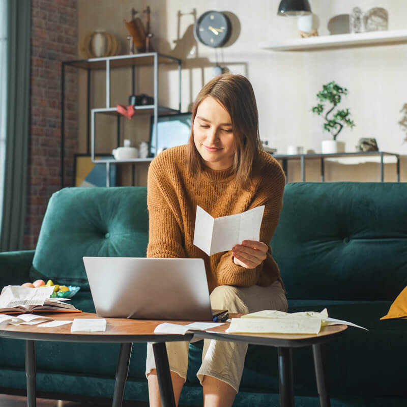 A woman sitting on a sofa entering figures into a computer.