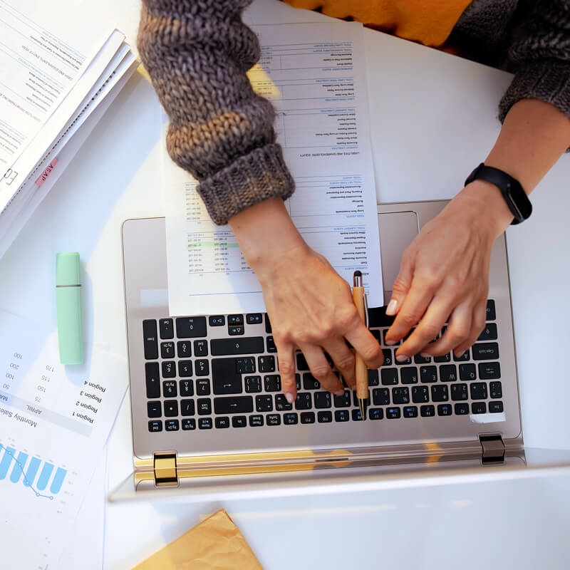 A person working on a laptop with graphs on a desk.