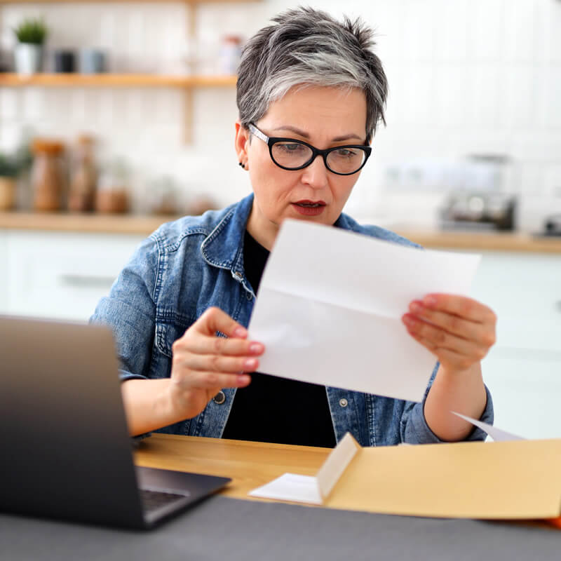 A middle-aged woman reviewing a bill in her kitchen.