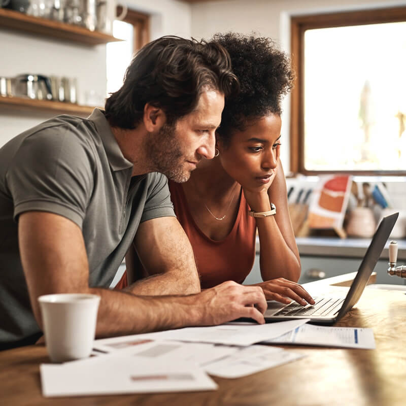 A couple reviews their finances on a laptop screen.