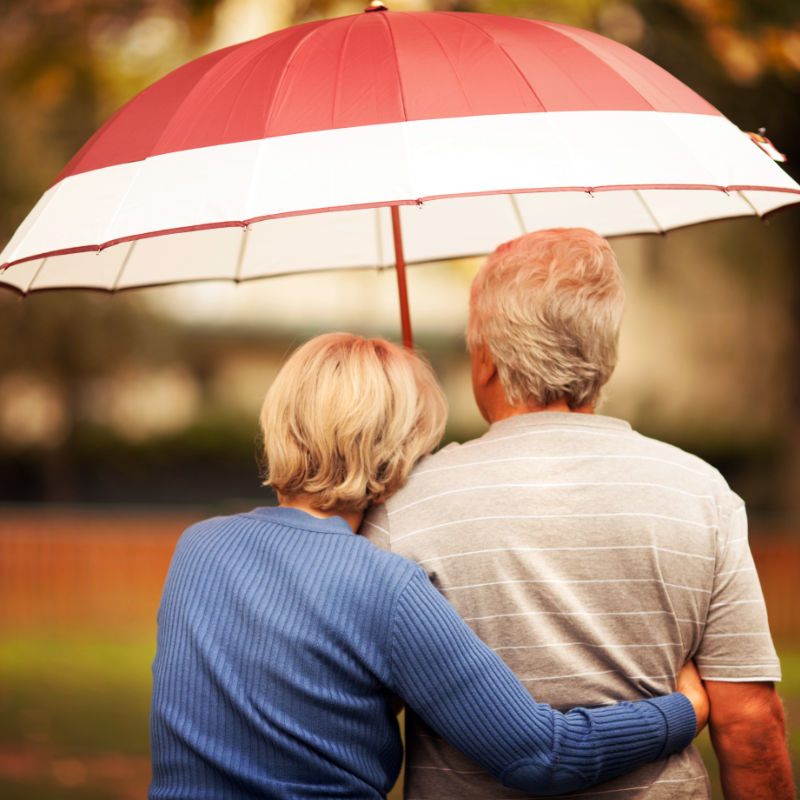 Older couple standing close under an umbrella.