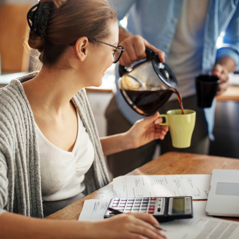 Woman doing finances at kitchen table. Partner pouring her coffee.