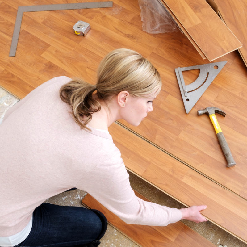 A woman installing a wood floor in a home.