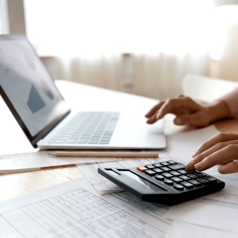 A close up on hands using a laptop and calculator.
