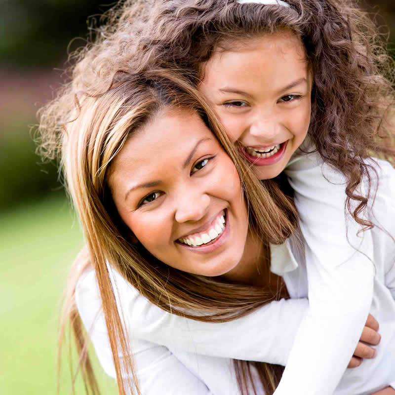 A woman giving a young girl a piggy back ride.