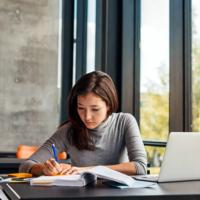 A college student writing notes at a desk in a library.