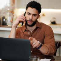 A serious man looking at his laptop while on the phone
