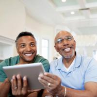 A smiling man and his father using a tablet device.
