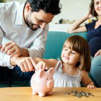 A young child putting money in a piggy bank as her parents watch.