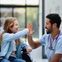 A doctor gives a high five to a girl in a wheelchair