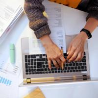 A person working on a laptop with graphs on a desk.