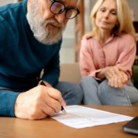 An older man signs a document.