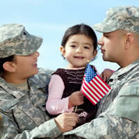 Military couple holding their toddler girl with small American flag.