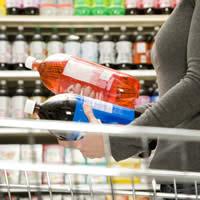 A woman comparing two soda bottles in a supermarket.