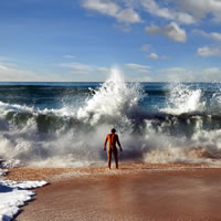 Man facing huge crashing waves on beach.